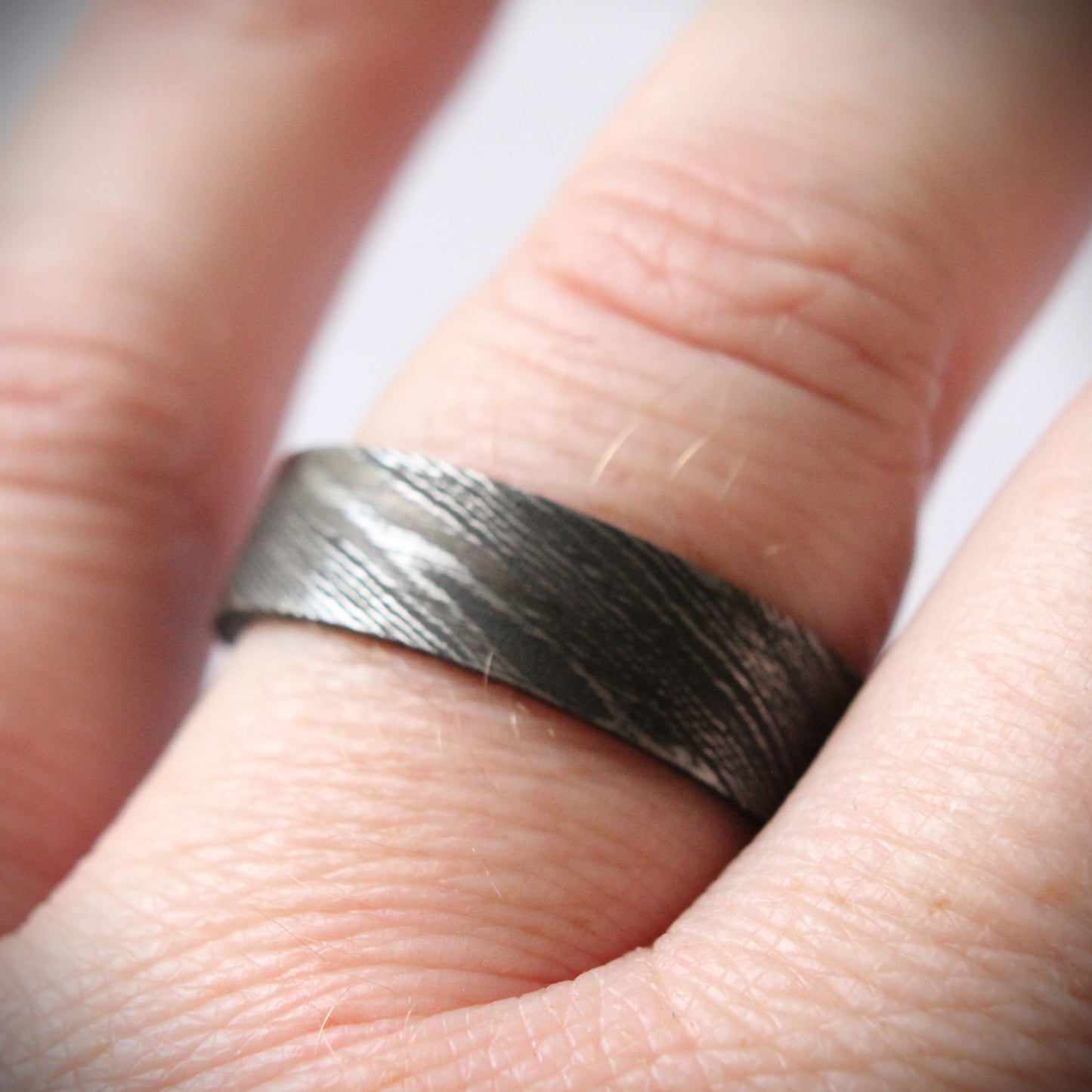 Stunning Damascus steel ring with intricate flowing patterns, heat-treated and blackened for a bold, modern look. The outer band features a unique, layered design with a dark, matte finish, combining strength and elegance in a one-of-a-kind piece of fine craftsmanship. Perfect for a wedding band, engagement ring, or statement piece.