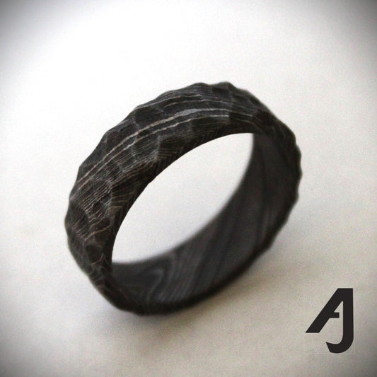 A rugged and bold Damascus steel ring with a 7mm-wide band, featuring intricate swirling patterns and a carved surface that mimics a mountain ridge. Each ring is uniquely forged, ensuring no two are exactly alike. A perfect blend of durability, artistry, and individuality.