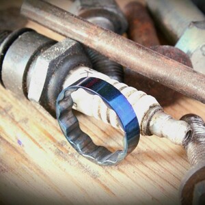 Blue Socket Ring, a unique piece of jewelry made from a 19mm mechanics socket. The ring features a sleek gunmetal blue finish with a ridged interior for comfort. Crafted from high-grade tool steel, it showcases an industrial design aesthetic, emphasizing durability and strength. The ring's distinctive look appeals to those with a bold, rugged style, representing a blend of sustainability and modern craftsmanship.